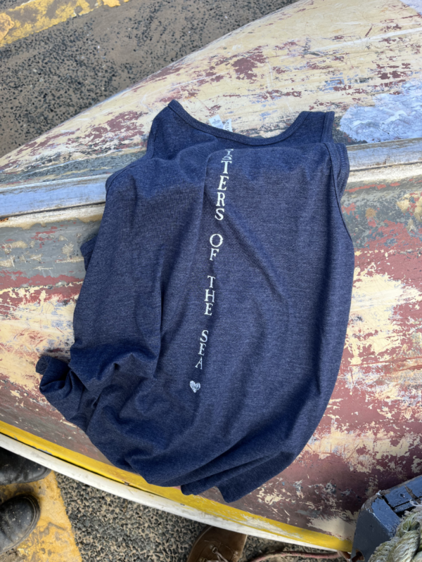 A blue Sisters of the Sea vest with a vertical logo down the back, draped on a battered-looking upturned boat.