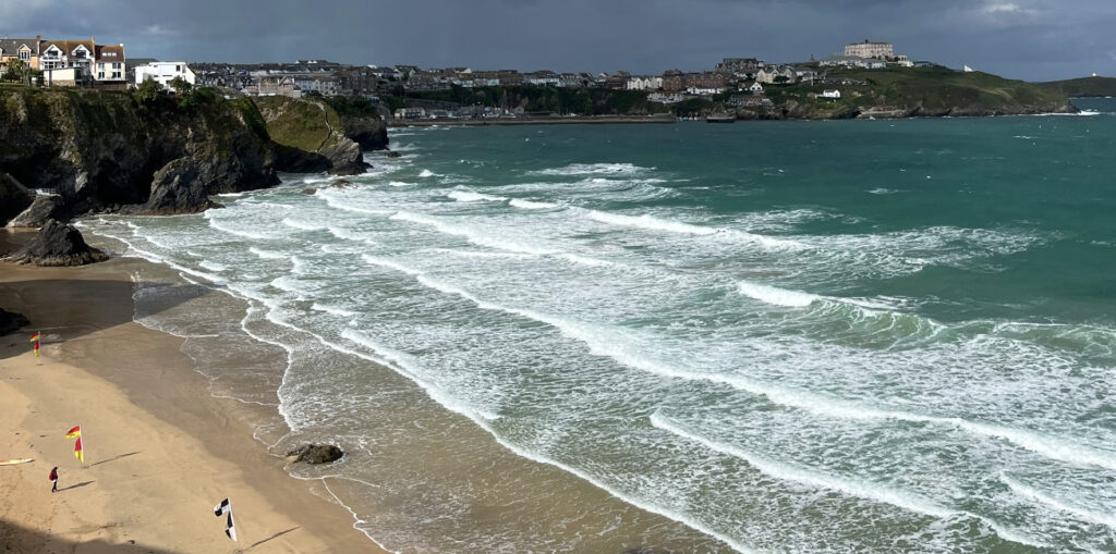 Surfing the white water:
A big beach with lots of white frothy white water breaking onto the sandy shore, with cliffs and the town in the background.