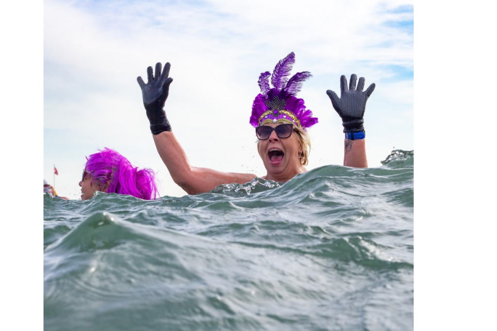 A lady in the sea with a beautiful purple feather tiara and her hands in the air. She looks happy and exhilarated.